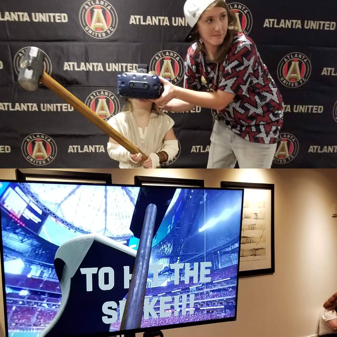 A VR scene of a young woman using a foamcore hammer to hit the golden spike in VR.